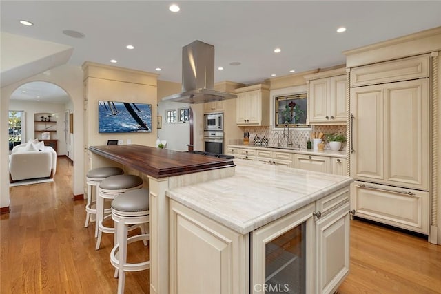 kitchen featuring island exhaust hood, cream cabinets, built in appliances, and light hardwood / wood-style floors