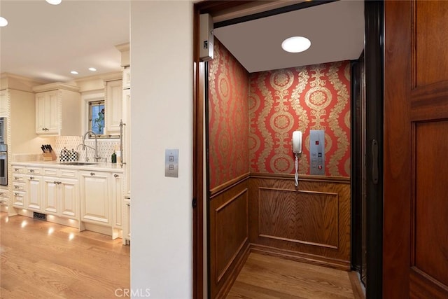 details with oven, sink, elevator, tasteful backsplash, and wood-type flooring