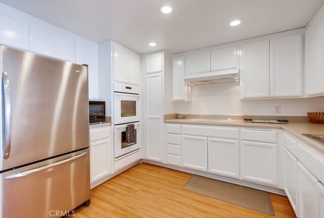 kitchen with stainless steel fridge, white double oven, white cabinetry, cooktop, and light wood-type flooring