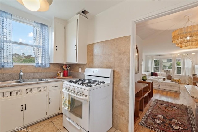 kitchen featuring a healthy amount of sunlight, sink, white range with gas stovetop, and white cabinets