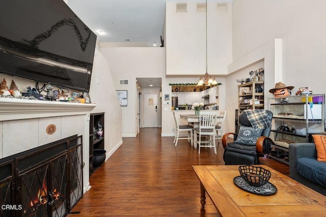 living room featuring dark wood-type flooring, a high ceiling, a notable chandelier, and a tiled fireplace