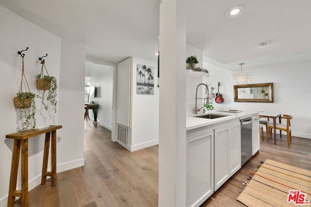 kitchen featuring pendant lighting, sink, light hardwood / wood-style flooring, stainless steel dishwasher, and white cabinetry