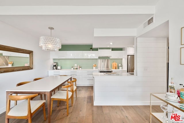 kitchen featuring white cabinetry, hanging light fixtures, a notable chandelier, light hardwood / wood-style floors, and decorative backsplash