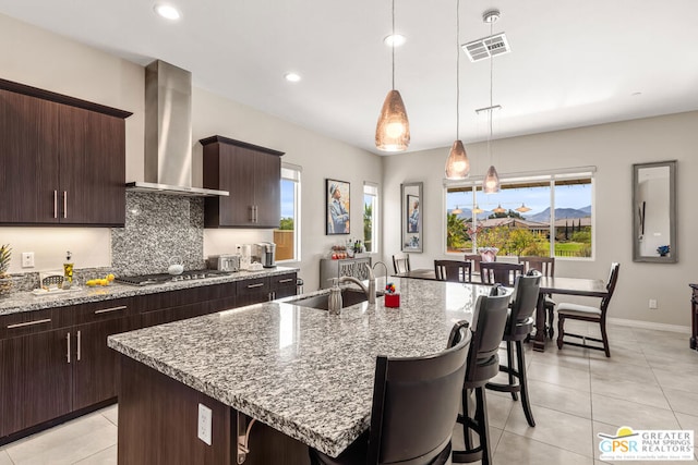 kitchen with stainless steel gas stovetop, wall chimney exhaust hood, sink, and a kitchen island with sink