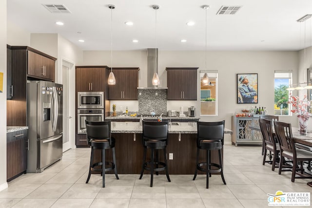 kitchen with dark brown cabinetry, hanging light fixtures, stainless steel appliances, and wall chimney range hood