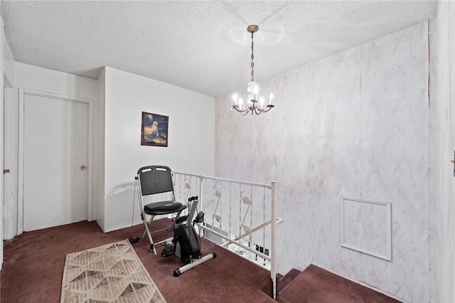 exercise room featuring a textured ceiling, an inviting chandelier, and dark carpet