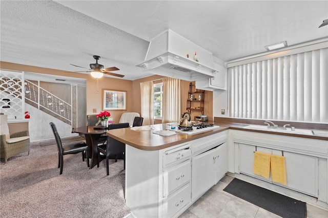 kitchen with kitchen peninsula, light carpet, custom exhaust hood, a textured ceiling, and white cabinets