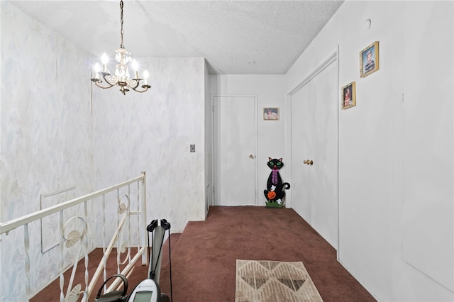 hall with dark colored carpet, a textured ceiling, and a chandelier