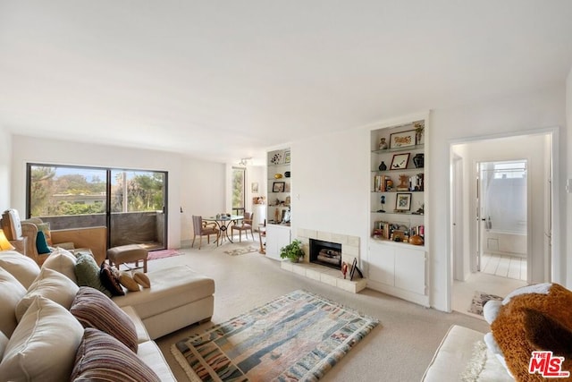 living room with built in shelves, light colored carpet, and a tiled fireplace