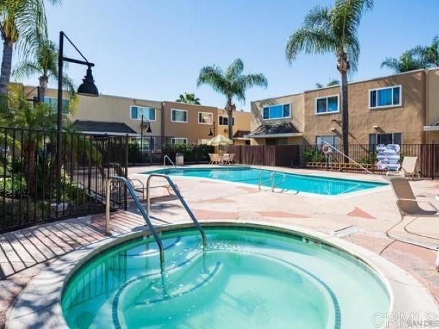 community pool featuring a community hot tub, a residential view, a patio area, and fence