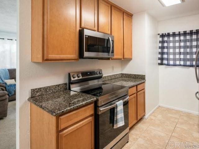 kitchen with brown cabinets, dark stone countertops, and stainless steel appliances