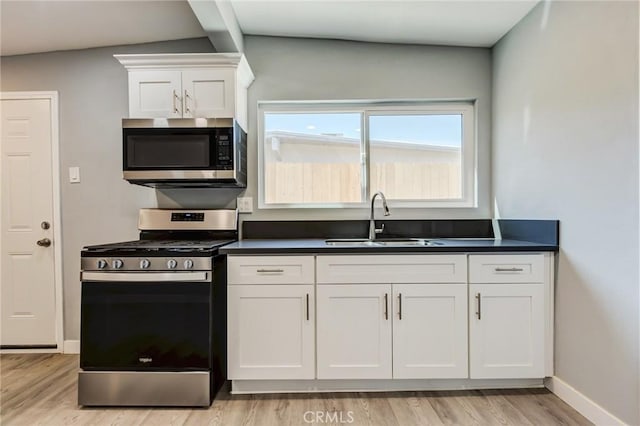 kitchen featuring lofted ceiling, white cabinets, sink, light wood-type flooring, and appliances with stainless steel finishes