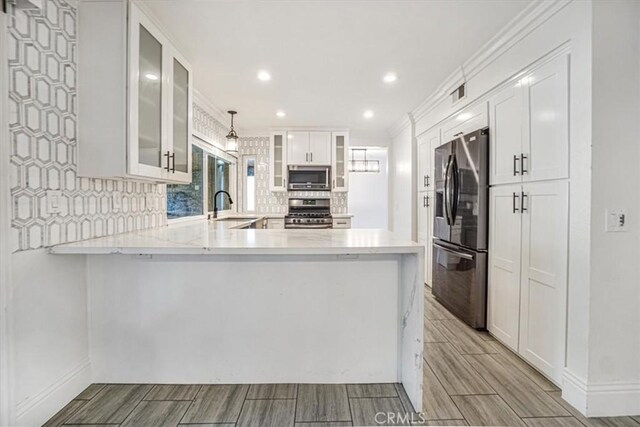 kitchen with pendant lighting, kitchen peninsula, sink, appliances with stainless steel finishes, and white cabinets