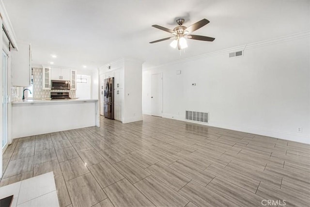 unfurnished living room featuring ceiling fan, crown molding, and sink