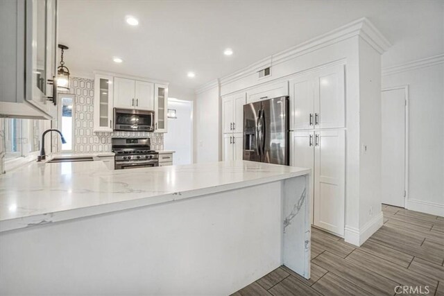 kitchen featuring white cabinetry, kitchen peninsula, stainless steel appliances, decorative light fixtures, and sink