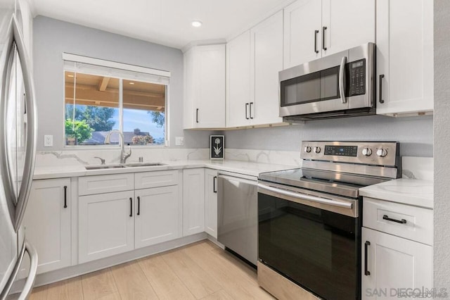 kitchen featuring light stone countertops, stainless steel appliances, sink, white cabinets, and light hardwood / wood-style floors