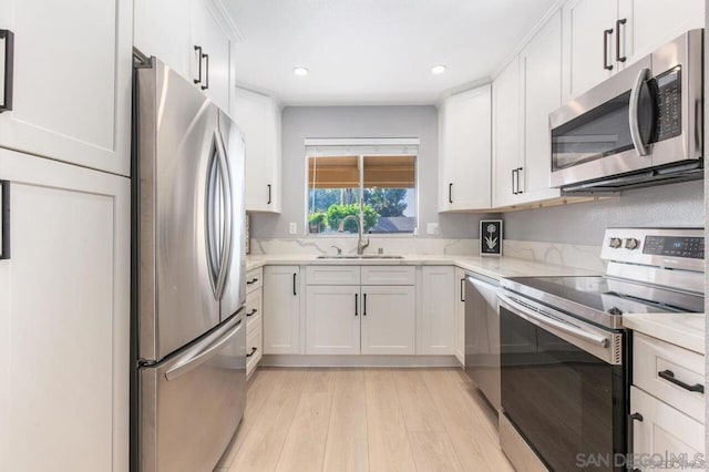 kitchen featuring appliances with stainless steel finishes, sink, white cabinets, light hardwood / wood-style flooring, and light stone counters