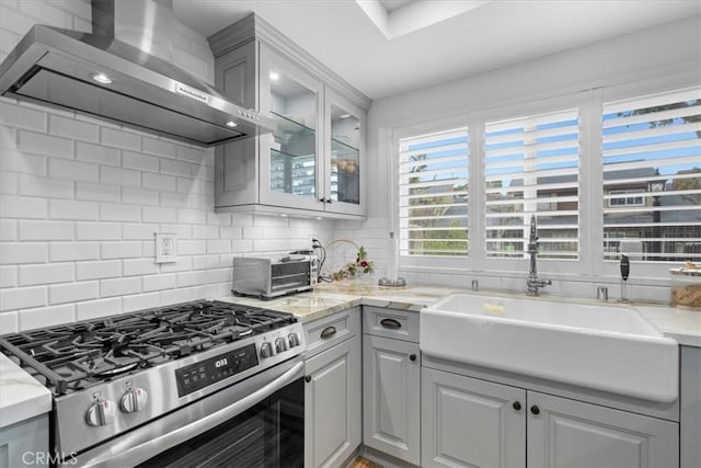 kitchen with sink, wall chimney range hood, tasteful backsplash, high end stove, and gray cabinets