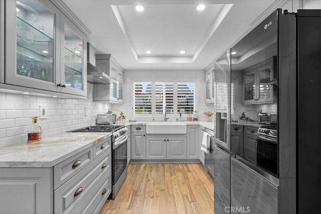 kitchen featuring sink, light hardwood / wood-style flooring, a tray ceiling, gray cabinets, and appliances with stainless steel finishes