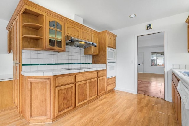 kitchen featuring white appliances, tile countertops, decorative backsplash, and light wood-type flooring