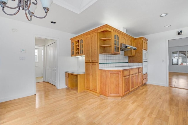 kitchen with a notable chandelier, black electric stovetop, decorative backsplash, and light hardwood / wood-style flooring