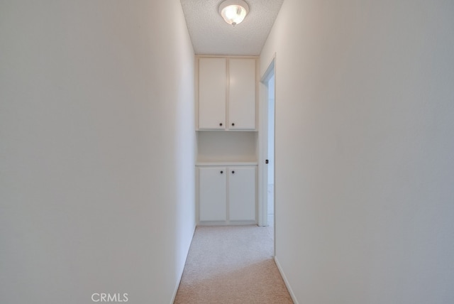 hallway with light carpet and a textured ceiling