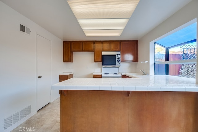 kitchen featuring tile counters, kitchen peninsula, sink, and stove