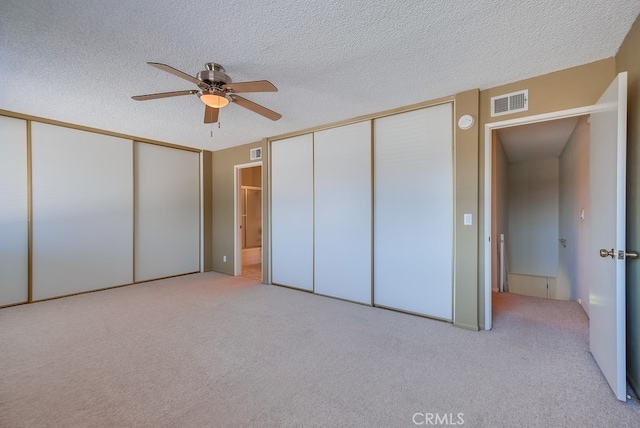 unfurnished bedroom with multiple closets, light colored carpet, a textured ceiling, and ceiling fan