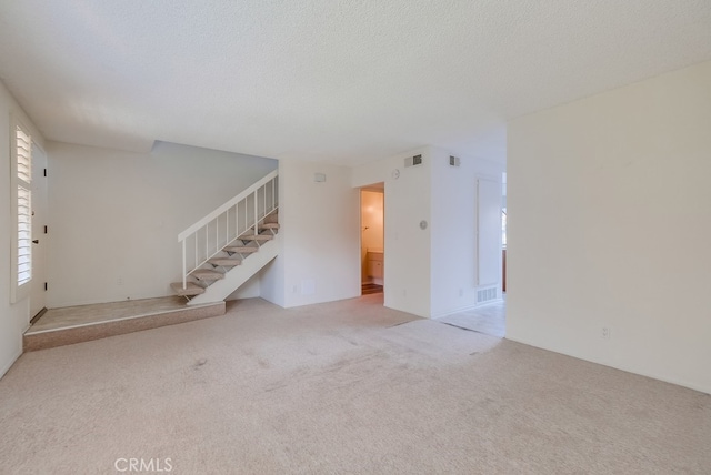 unfurnished living room with light colored carpet and a textured ceiling