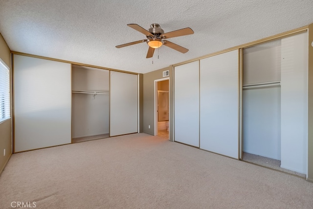 unfurnished bedroom featuring multiple closets, ceiling fan, light colored carpet, and a textured ceiling