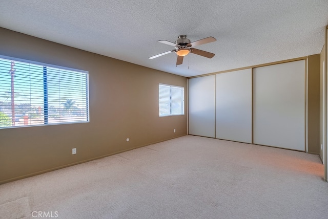 unfurnished bedroom featuring multiple windows, ceiling fan, light colored carpet, and a textured ceiling