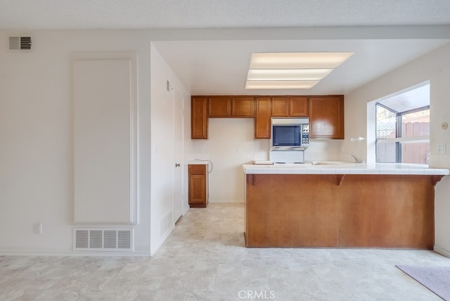 kitchen with tile counters, kitchen peninsula, and a textured ceiling