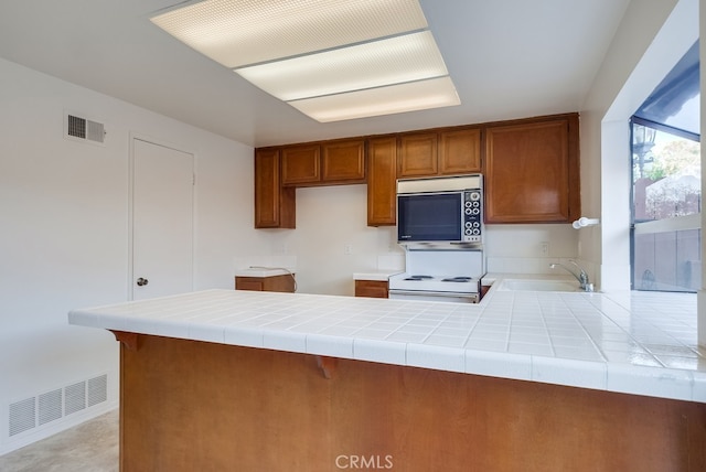 kitchen featuring sink, tile counters, white electric stove, and kitchen peninsula