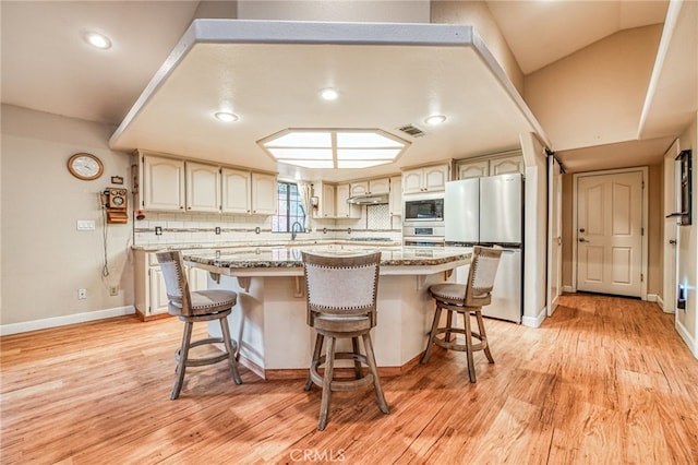 kitchen with a kitchen bar, light stone countertops, light wood-type flooring, backsplash, and stainless steel appliances