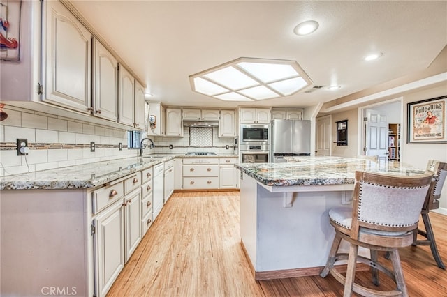 kitchen featuring light stone countertops, appliances with stainless steel finishes, a kitchen breakfast bar, tasteful backsplash, and light hardwood / wood-style flooring