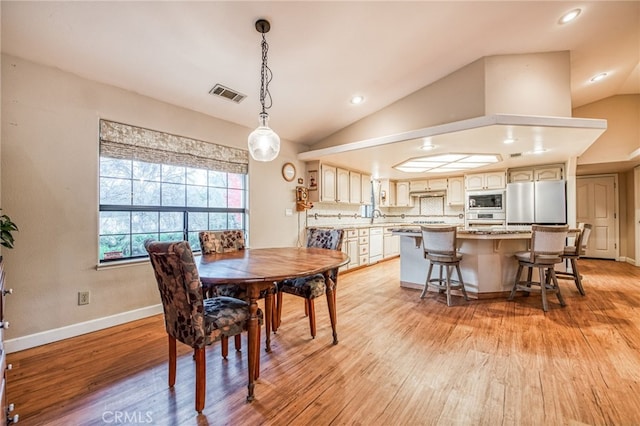 dining area with light wood-type flooring, sink, and vaulted ceiling