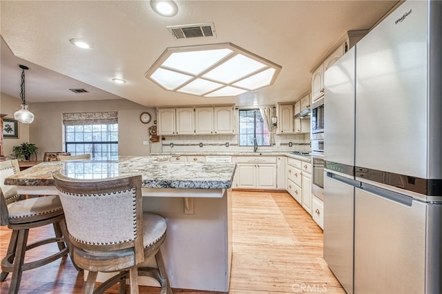 kitchen with backsplash, a healthy amount of sunlight, stainless steel appliances, and light wood-type flooring