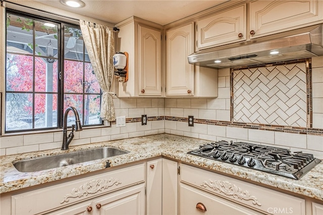 kitchen with backsplash, light stone counters, stainless steel gas cooktop, and sink