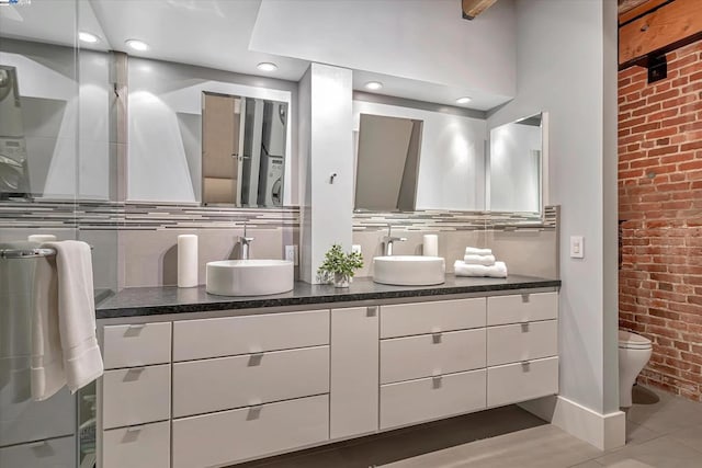 bathroom with tile patterned flooring, vanity, toilet, and brick wall