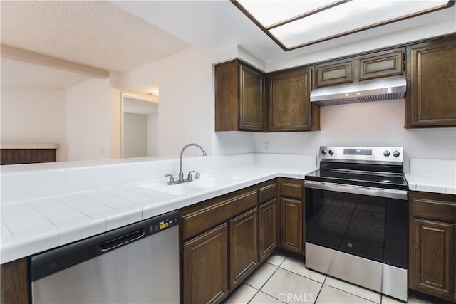 kitchen featuring tile counters, dark brown cabinetry, sink, and appliances with stainless steel finishes