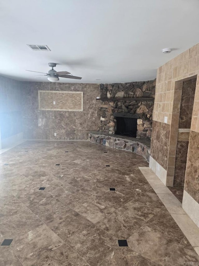 unfurnished living room featuring ceiling fan and a stone fireplace