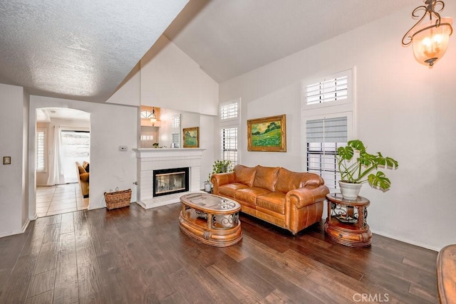 living room featuring dark hardwood / wood-style flooring, a textured ceiling, high vaulted ceiling, a notable chandelier, and a fireplace