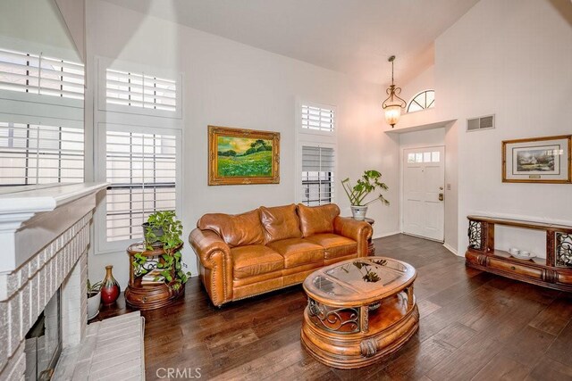 living room featuring a notable chandelier, dark hardwood / wood-style flooring, high vaulted ceiling, and a brick fireplace