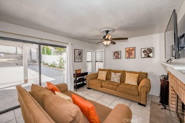 living room featuring ceiling fan, a textured ceiling, light tile patterned flooring, and a fireplace