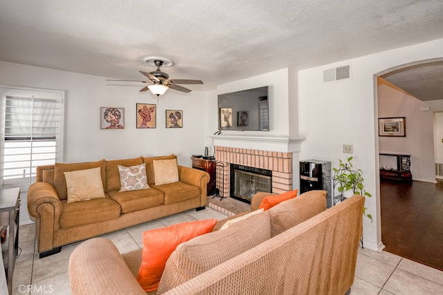 living room featuring ceiling fan, a fireplace, light wood-type flooring, and a textured ceiling