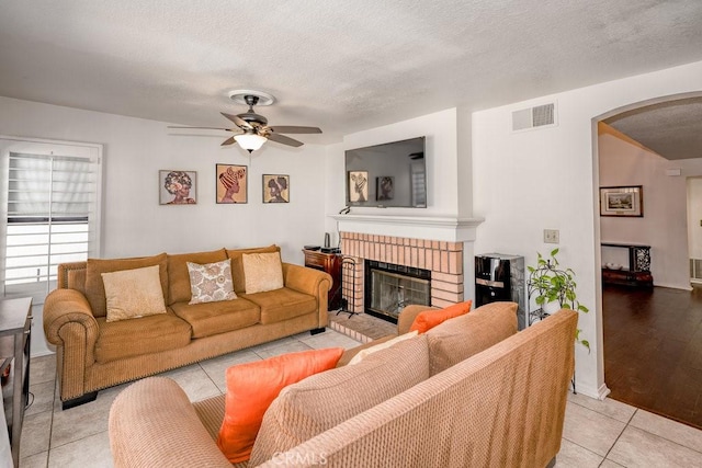 living area with arched walkways, visible vents, a brick fireplace, and a textured ceiling