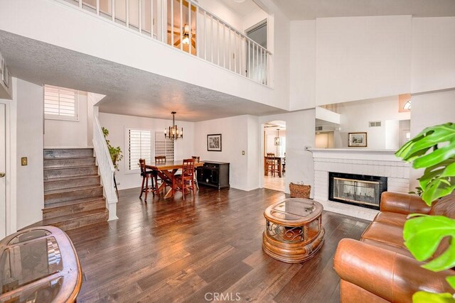 living room with a high ceiling, dark hardwood / wood-style flooring, a textured ceiling, and a brick fireplace