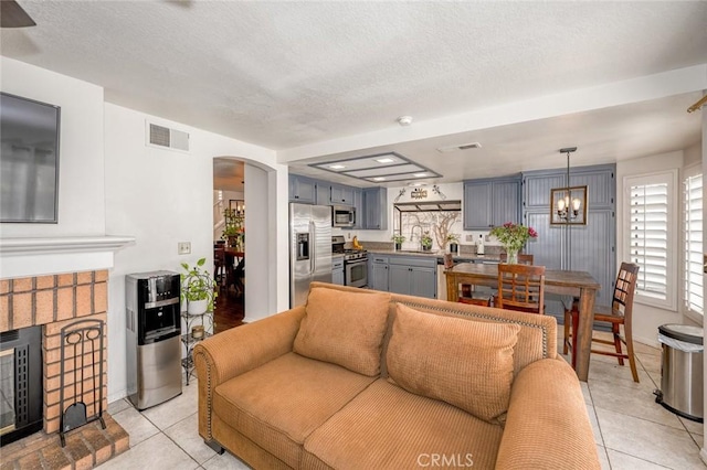 living room featuring arched walkways, light tile patterned floors, a brick fireplace, and a textured ceiling