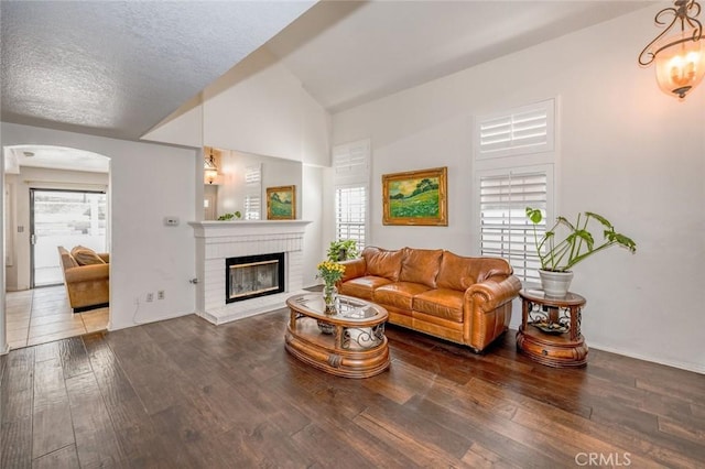 living room featuring lofted ceiling, a fireplace, arched walkways, a textured ceiling, and wood-type flooring