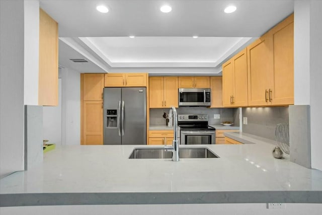 kitchen with sink, a raised ceiling, kitchen peninsula, light brown cabinetry, and appliances with stainless steel finishes